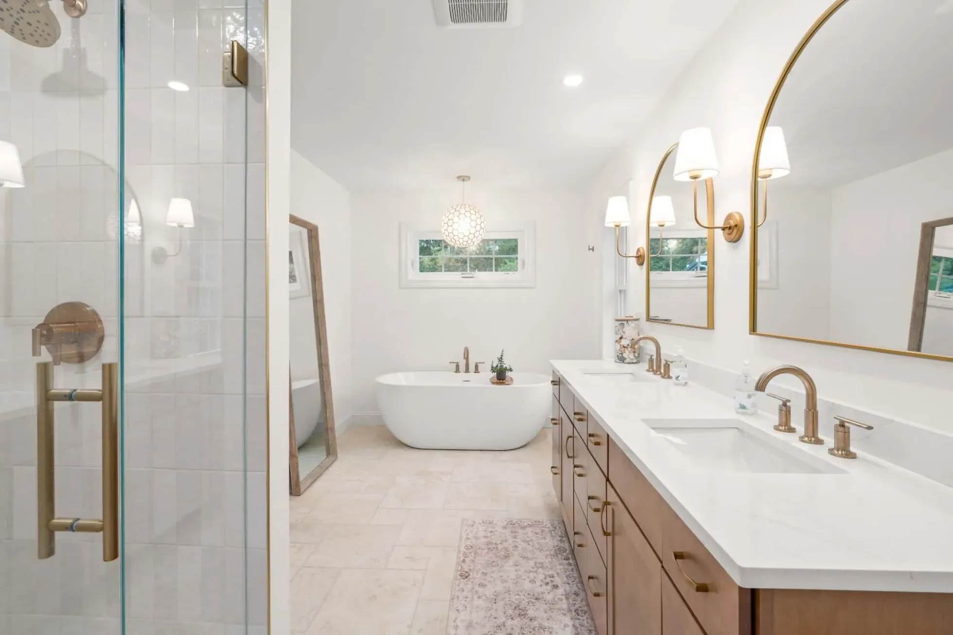 Primary bath with a long maple double vanity, arched brass mirrors and a freestanding tub