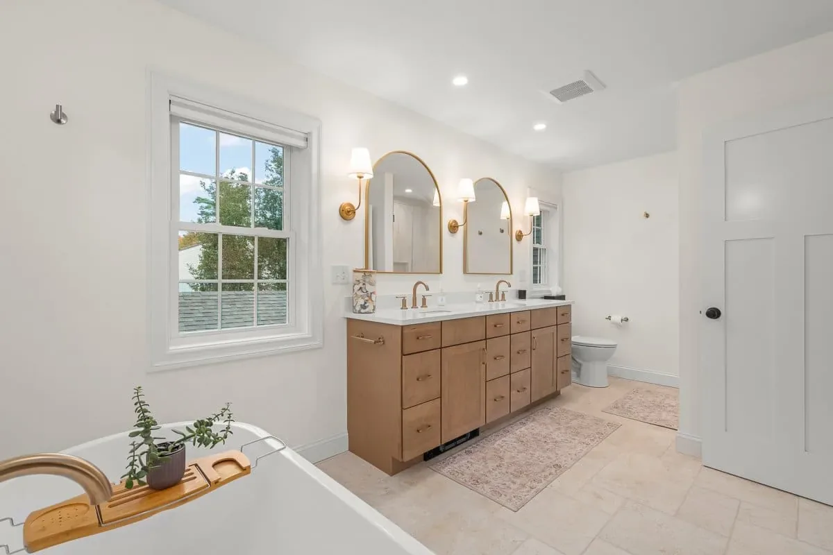 Primary bath with a window over the tub, maple vanity and arched mirrors