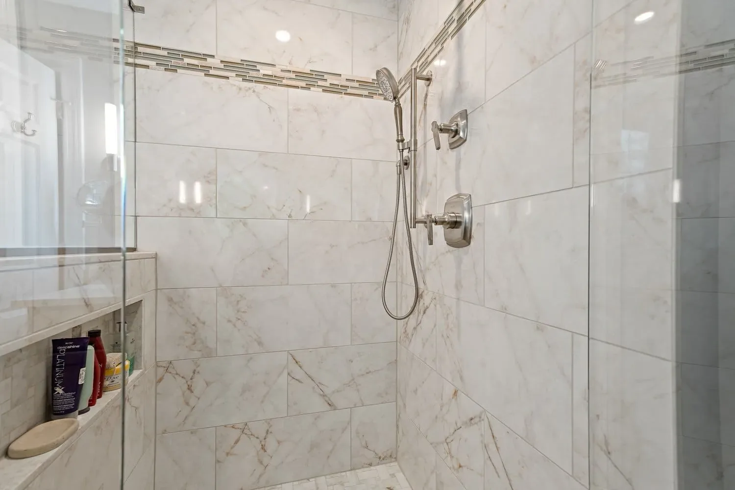 Walk-in shower with large-format porcelain tile, a decorative accent band and a recessed niche, Boxford MA primary bath