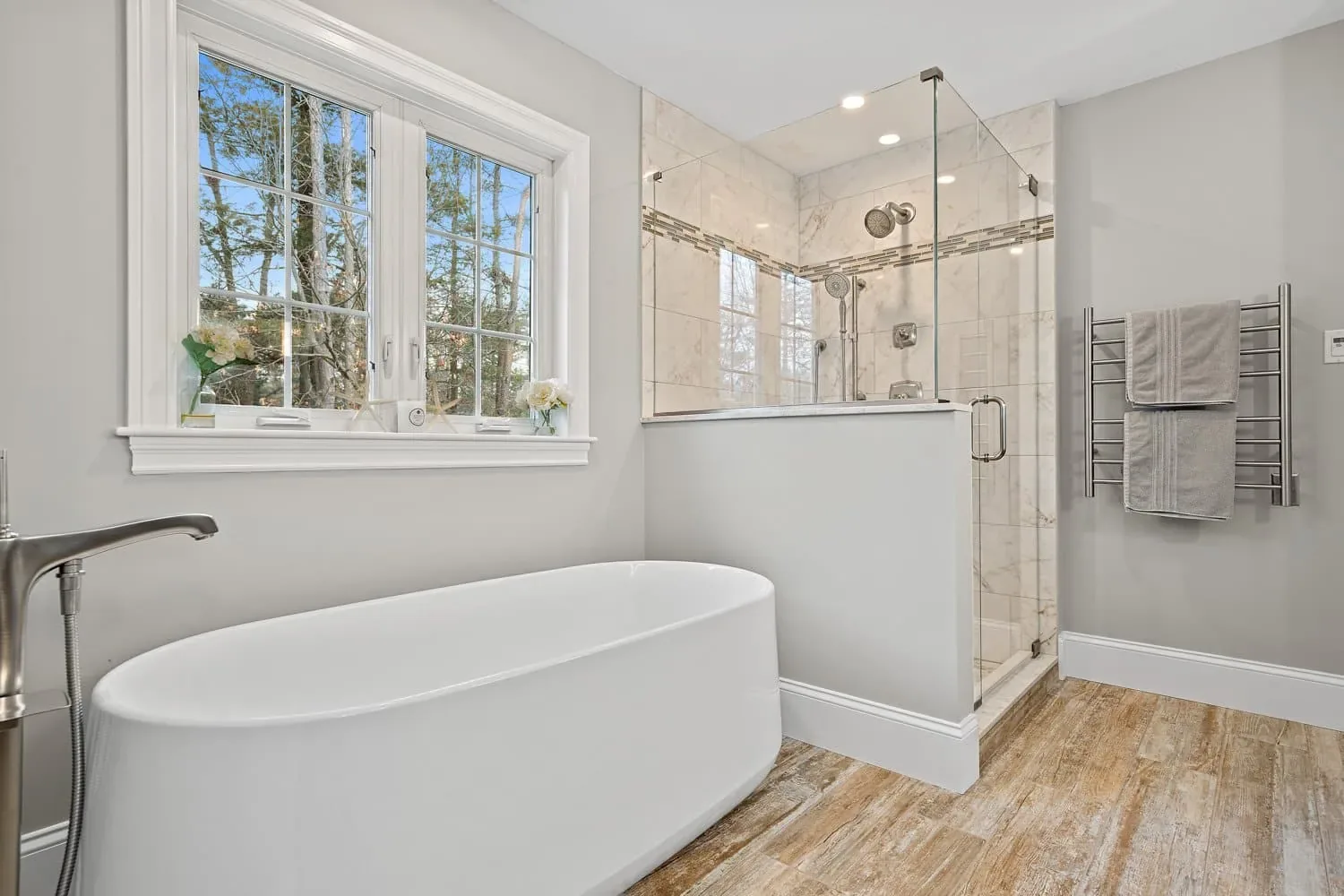 Freestanding soaking tub by the window beside the glass shower and a heated towel warmer