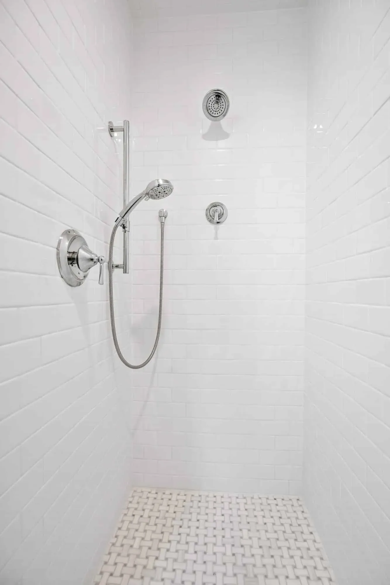 Floor-to-ceiling white tile shower with a handheld spray and mosaic floor