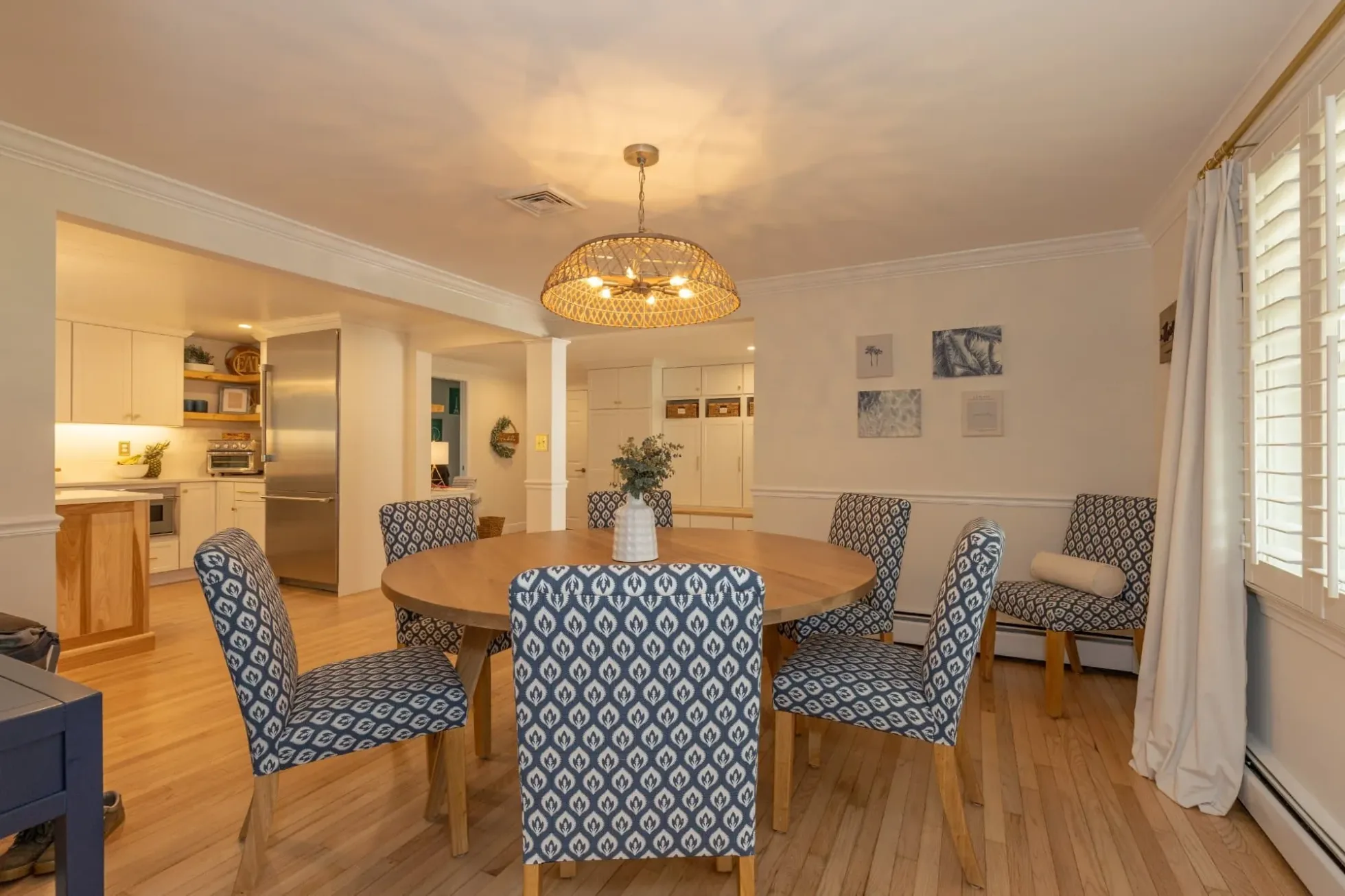 Dining area with a round table and a woven pendant, open to the kitchen