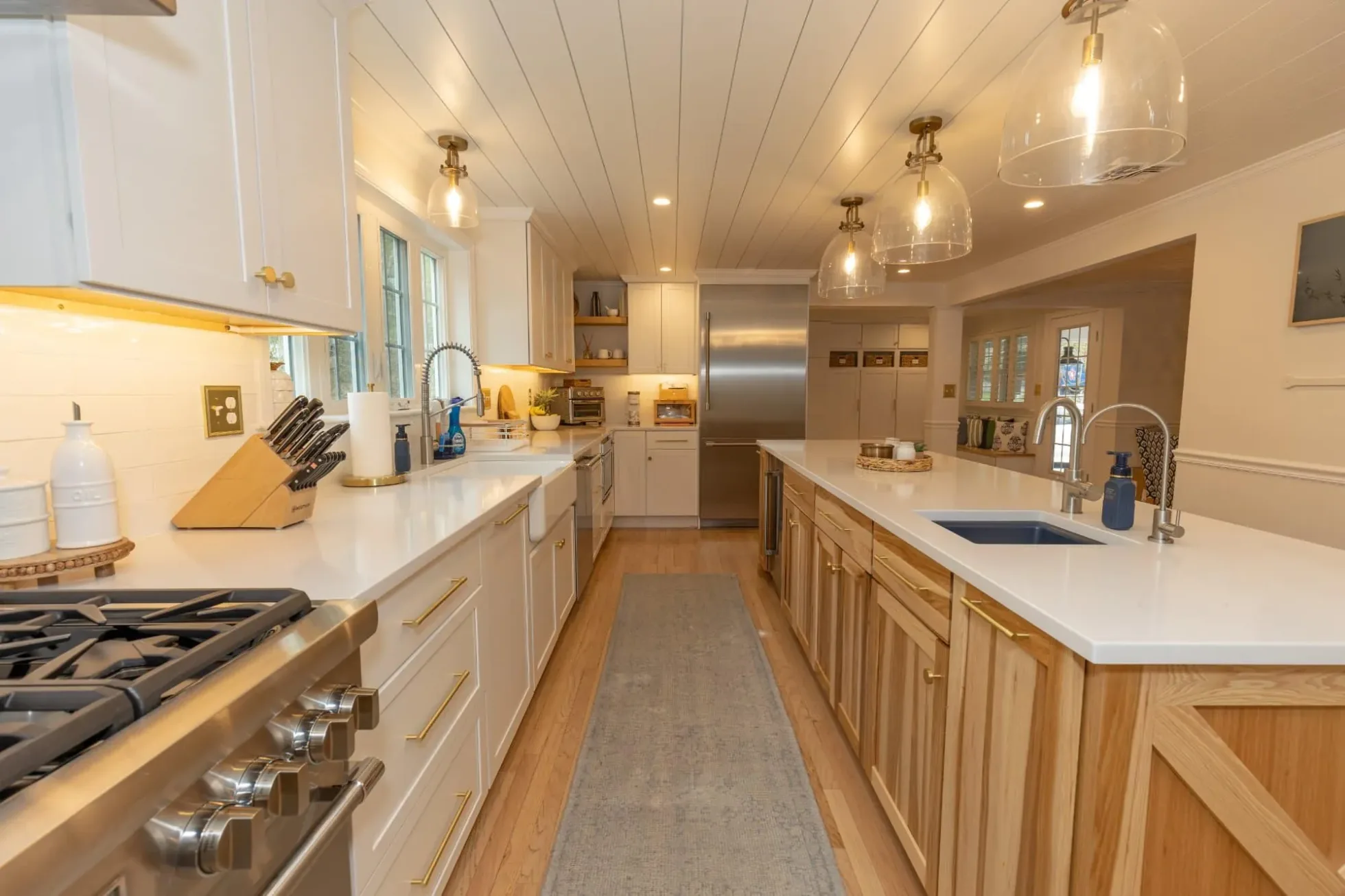 Long kitchen with a white oak clad island under a shiplap ceiling and glass pendants, Andover MA coastal renovation