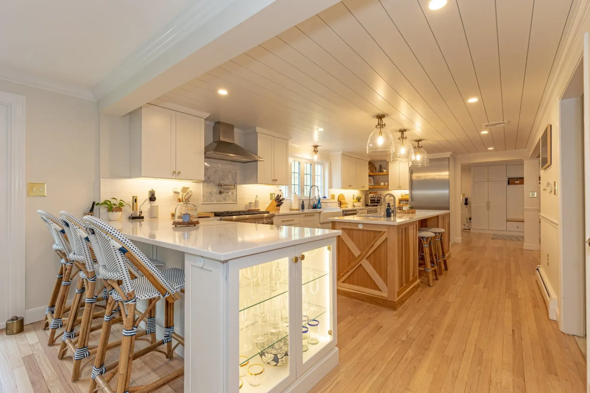 Dual kitchen islands, one with lit glass display cabinets and woven stools