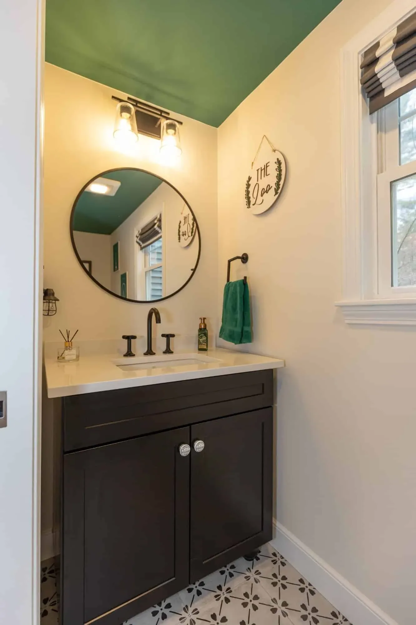 Powder room with a dark vanity, round mirror, patterned porcelain floor and painted green ceiling
