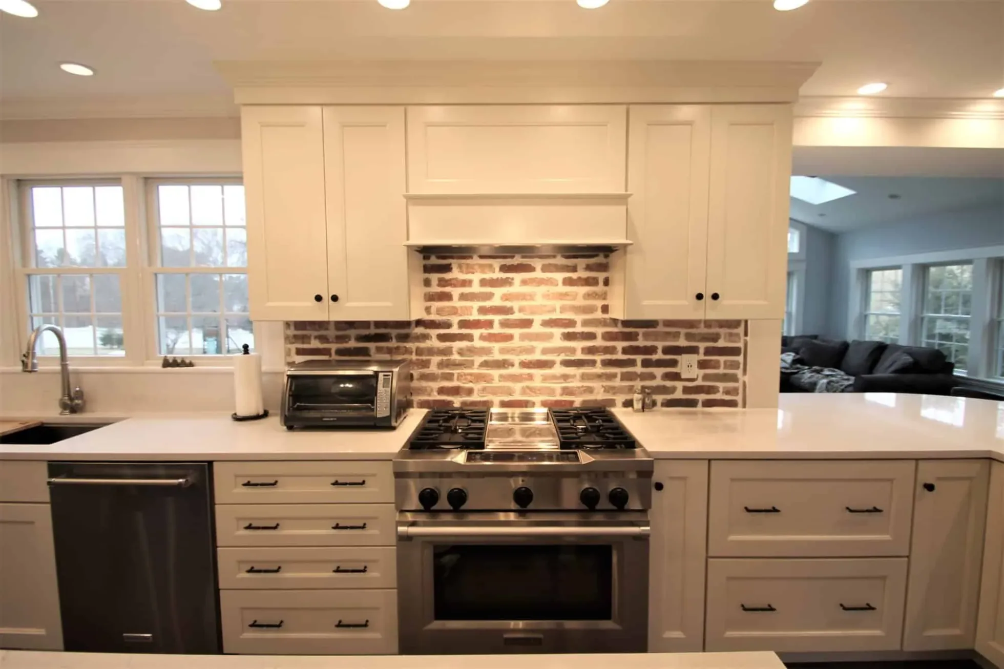 Exposed brick backsplash behind a professional gas range with a custom hood surround, Groveland MA
