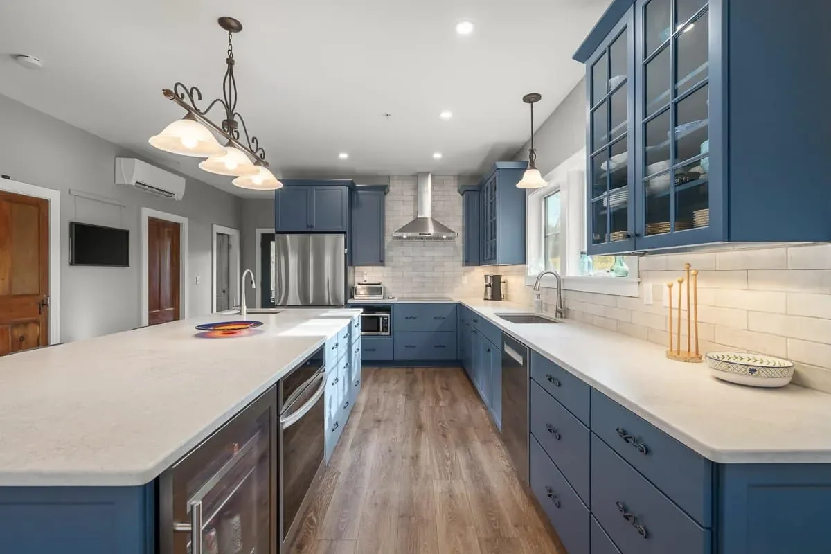 Quartz counters and blue cabinetry with glass-front uppers along the kitchen