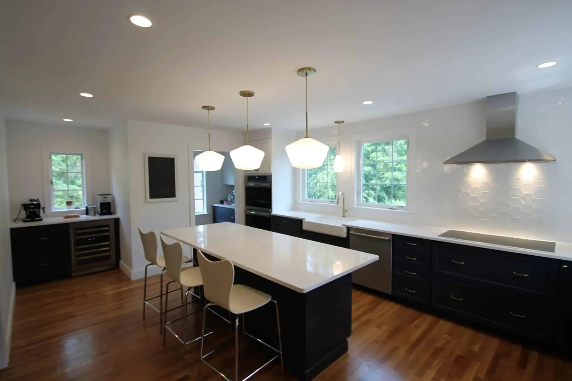 Stainless wall-mounted range hood over the induction cooktop, beverage fridge at the far end