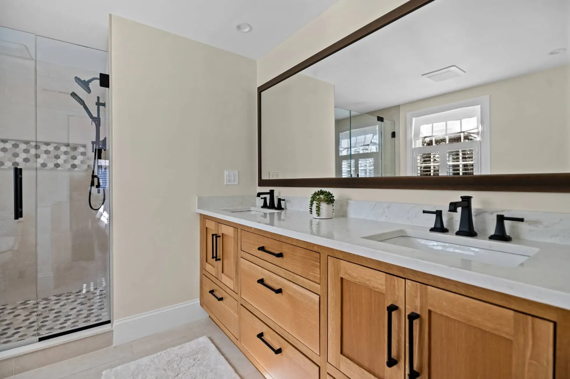 Primary bath with a white oak vanity, quartz top, matte black faucets and a glass shower