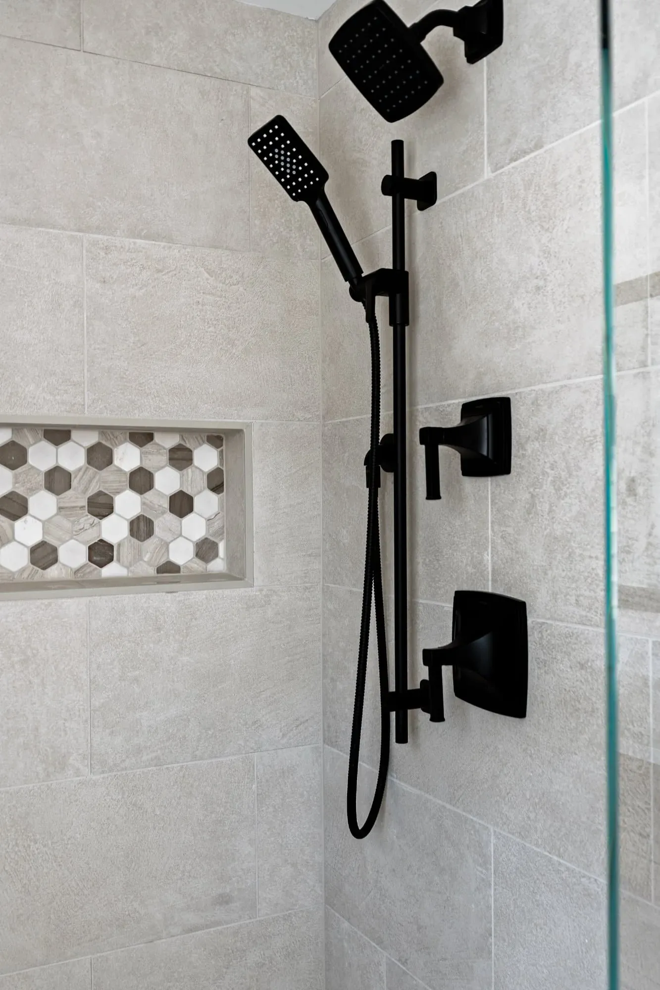 Matte black rain head and handheld shower fixtures with a mosaic niche