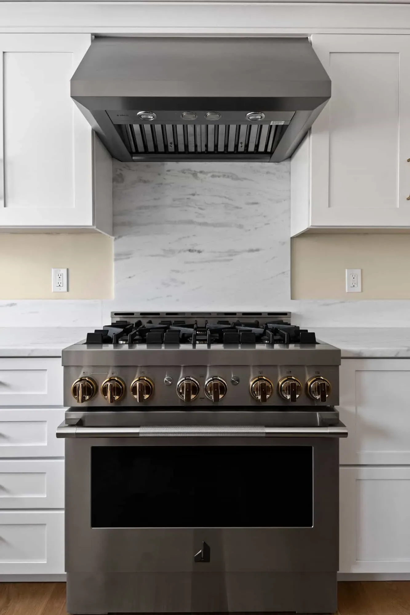 Stainless range hood over the gas range and marble-look backsplash