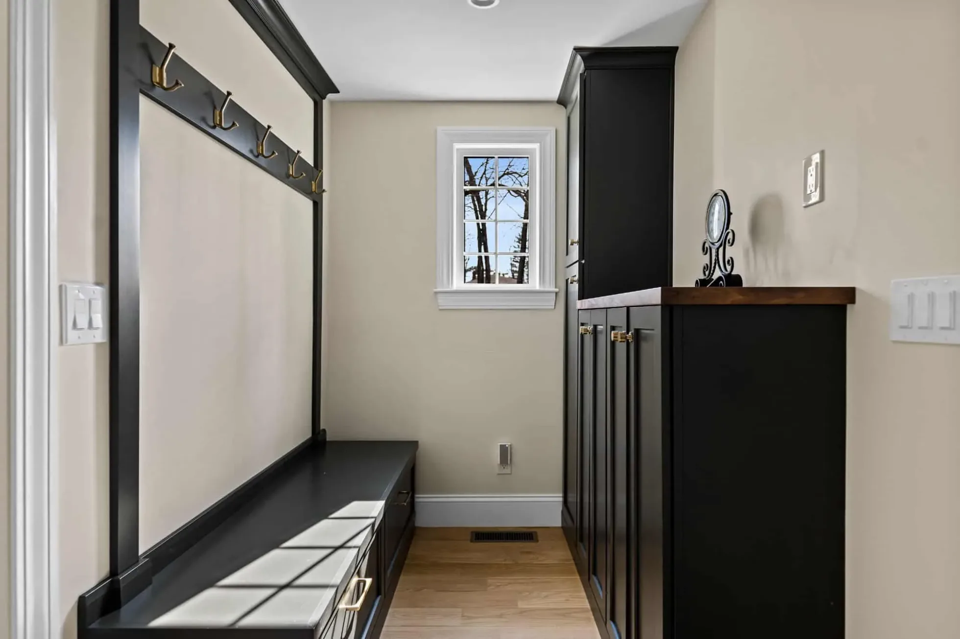 Mudroom with a built-in bench, hooks and tall dark storage cabinets