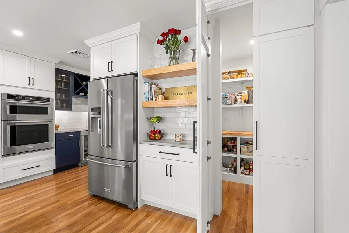Stainless refrigerator beside open shelving and a pantry, white shaker cabinets