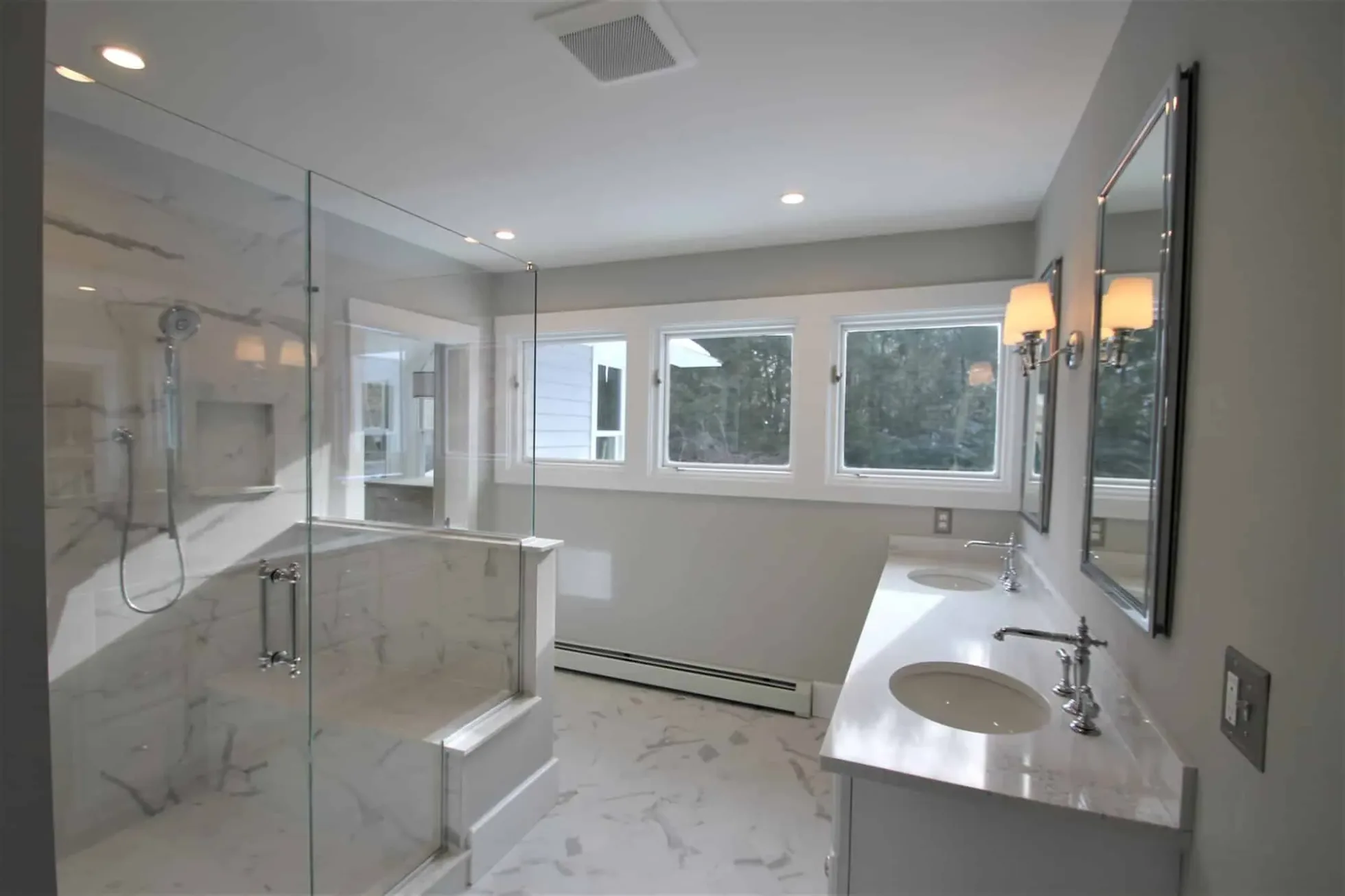 Primary bath with a frameless glass walk-in shower, marble-look porcelain and a row of windows