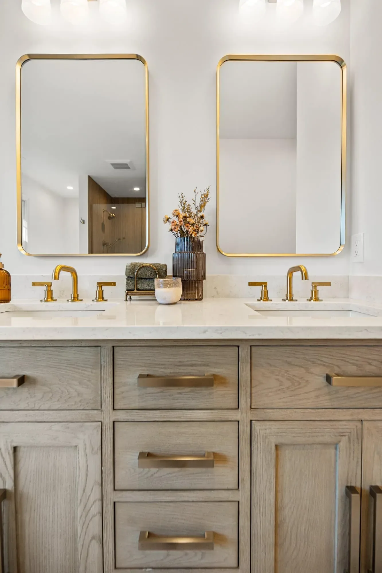 White oak vanity drawers with brass pulls and backlit mirror above