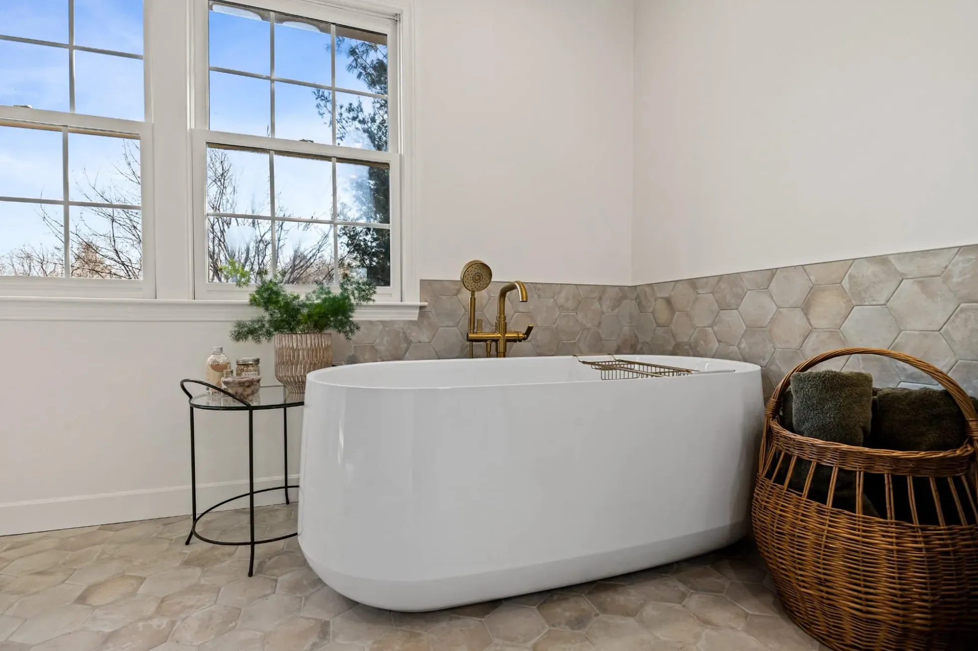 Freestanding soaking tub with a brushed brass floor-mounted filler under two windows