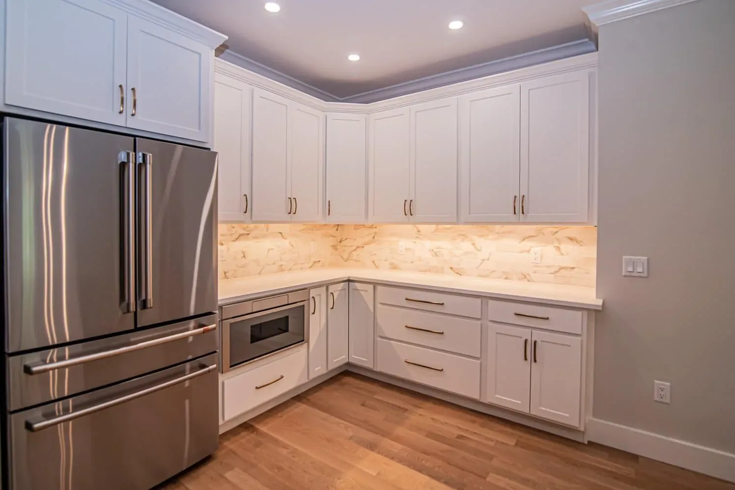 L-shaped run of white cabinets with under-cabinet lighting, Newton NH custom home