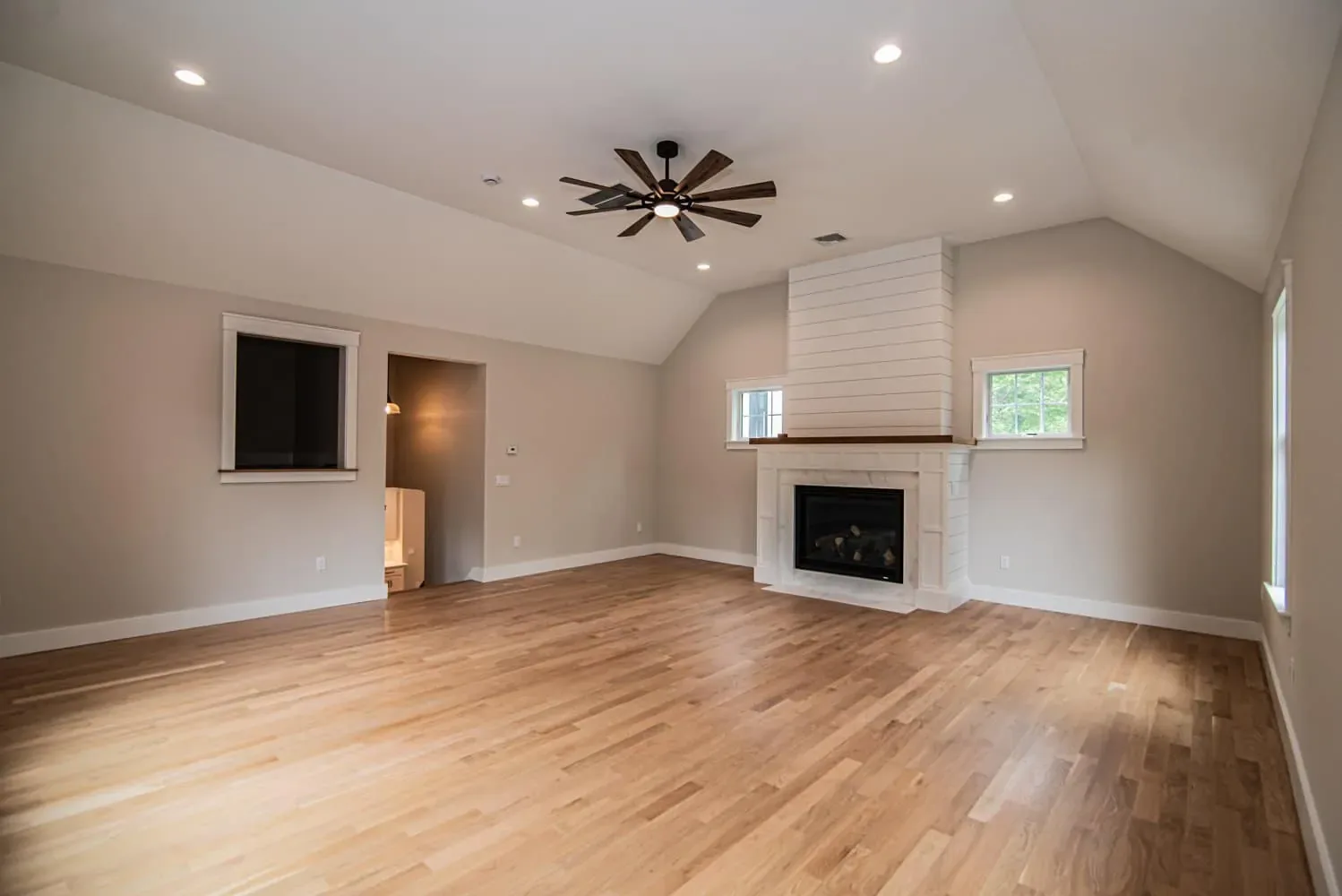 Room with a sloped ceiling, ceiling fan and a white fireplace surround, Newton NH custom home