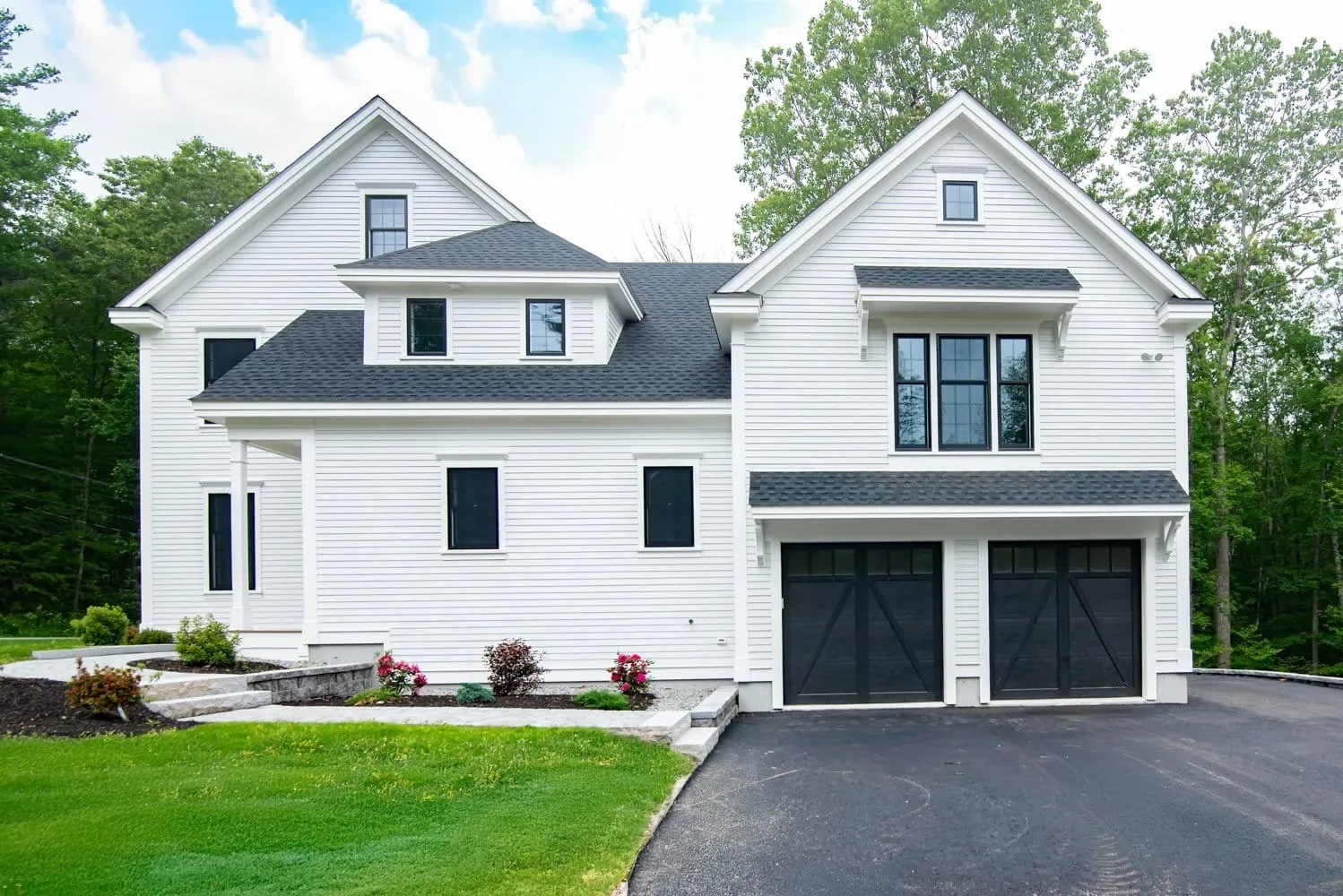 White farmhouse custom home with black windows, front gables and an attached two-car garage, Newton NH
