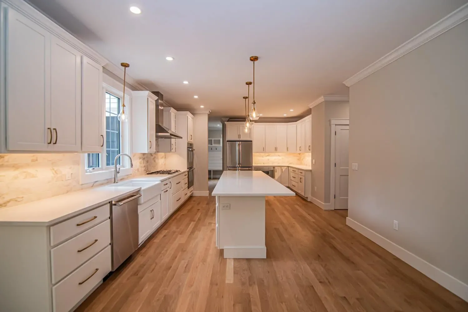Long white kitchen with a center island, pendant lights and hardwood floors, Newton NH custom home
