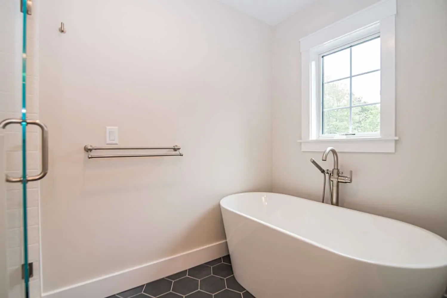 Primary bath with a freestanding soaking tub and black hexagon floor tile, Newton NH