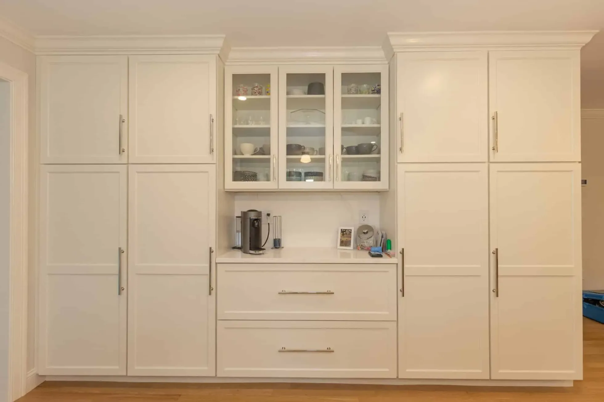 Full-height pantry and storage wall with glass-front cabinets and a coffee counter